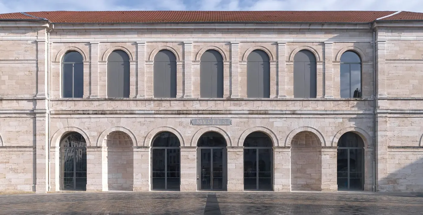 Photo d'une façade de musée en pierre : deux niveaux, rez-de-chaussée à arcades, baies cintrées à l'étage