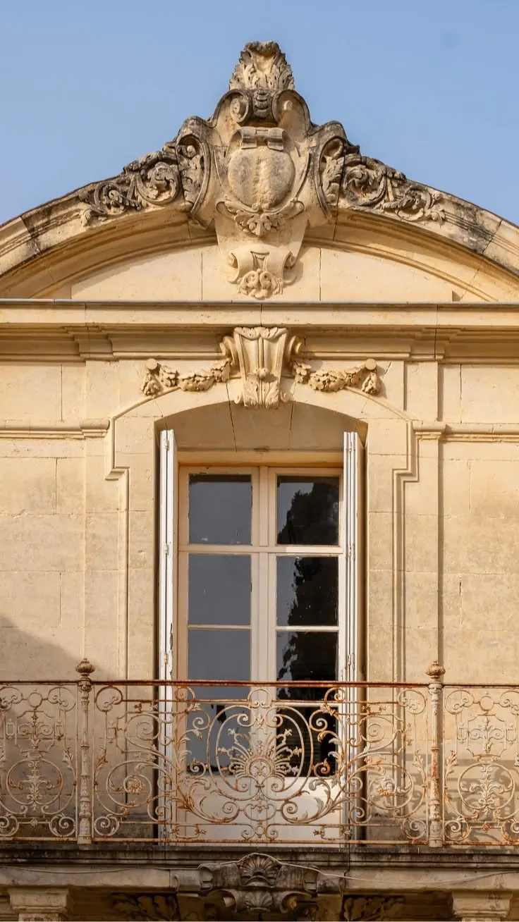 Photo rapprochée d'une travée en pierre : fenêtre cintrée, cartouche sculpté au fronton et garde-corps en ferronnerie rouillée