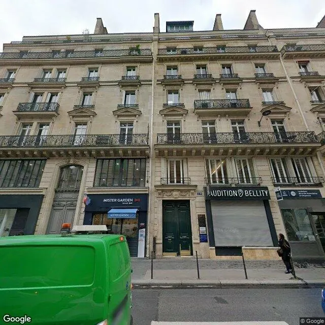 Vue Street View d'un immeuble de rapport en pierre : balcons filants, fenêtres à persiennes, boutiques au rez-de-chaussée